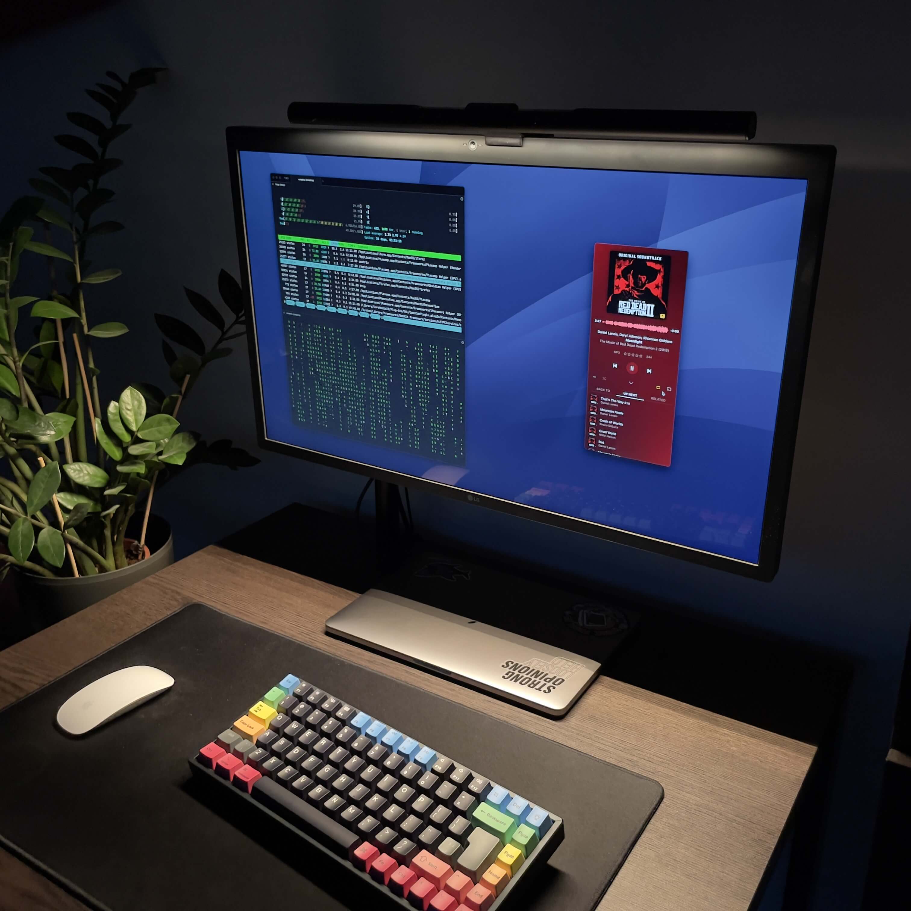 Photo showing my desk from a top right angle. The ScreenBar lamp is turned on and shines a bright light across the desk. The monitor shows a terminal and music player. Mouse and keyboard are layed out before the monitor.